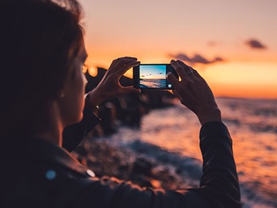 Photo of woman taking landscape photo of beach at sunset. 